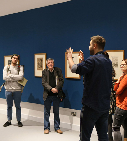 Grupa osób zwiedza wystawę z osobą prowadzącą