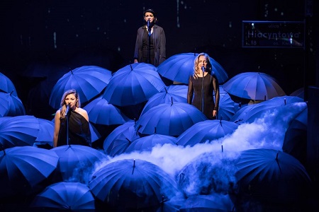 Aktorki na scenie w trakcie spektaklu, wokół nich parasolki