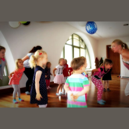 Częściowo nieostre zdjęcie z zajęć Strefa Zabawy. Roztańczone dzieci bawią się pod opieką instruktorki.