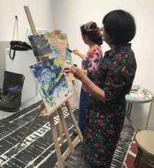 Dwie kobiety malujące obrazy na sztalugach.