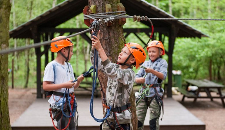 Dzieci w parku linowym, wspinające się po przeszkodach.