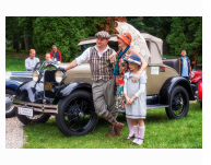 Zdjęcie rodziny (mężczyzna, kobieta i córka) ubranych w stylu epoki międzywojnia, w tle zabytkowe auto.