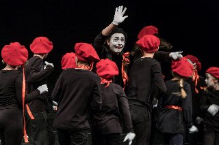 grupa dzieci w czarnych koszulkach i czerwonych beretach wraz z aktorem z umalowana na biało twarzą