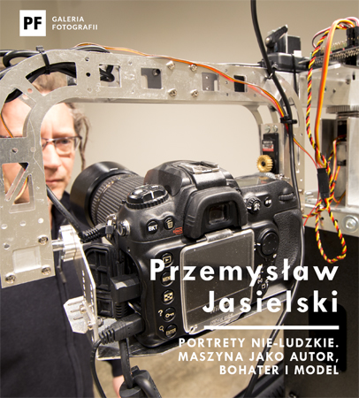W centralnej części zdjęcia widać maszynę fotografującą. W tle stoi mężczyzna w okularach i wpatruje się w obiektyw. W prawym dolnym rogu widnieje tytuł wystawy i nazwisko autora.