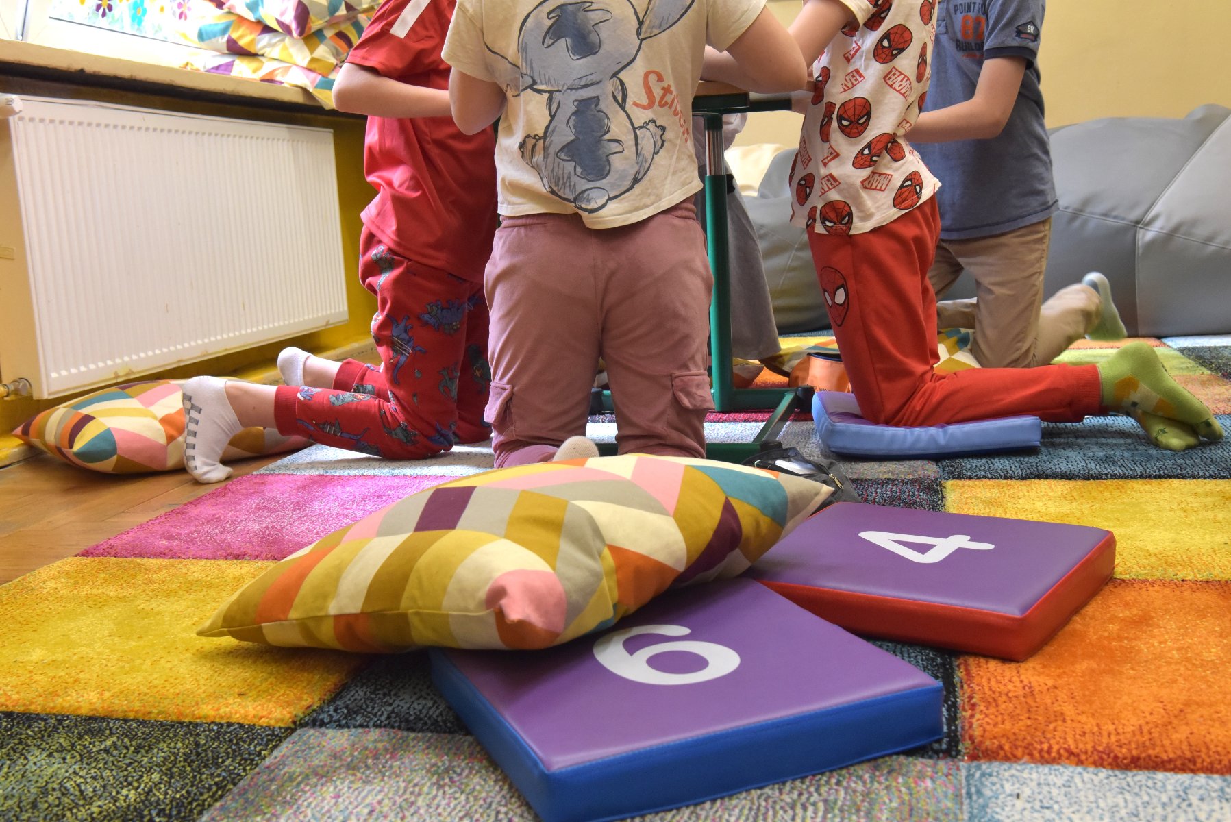 Zdjęcie przedstawia dzieci siedzące na pufie. Widać tylko ich nogi.