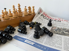 Zdjęcie przedstawia gazetę Senioralny Poznań oraz drewniane szachy