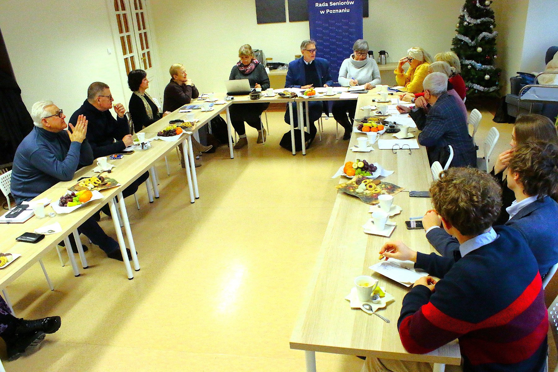 Zdjęcie przedstawia grupę seniorek i seniorów, którzy siedzą przy stole.