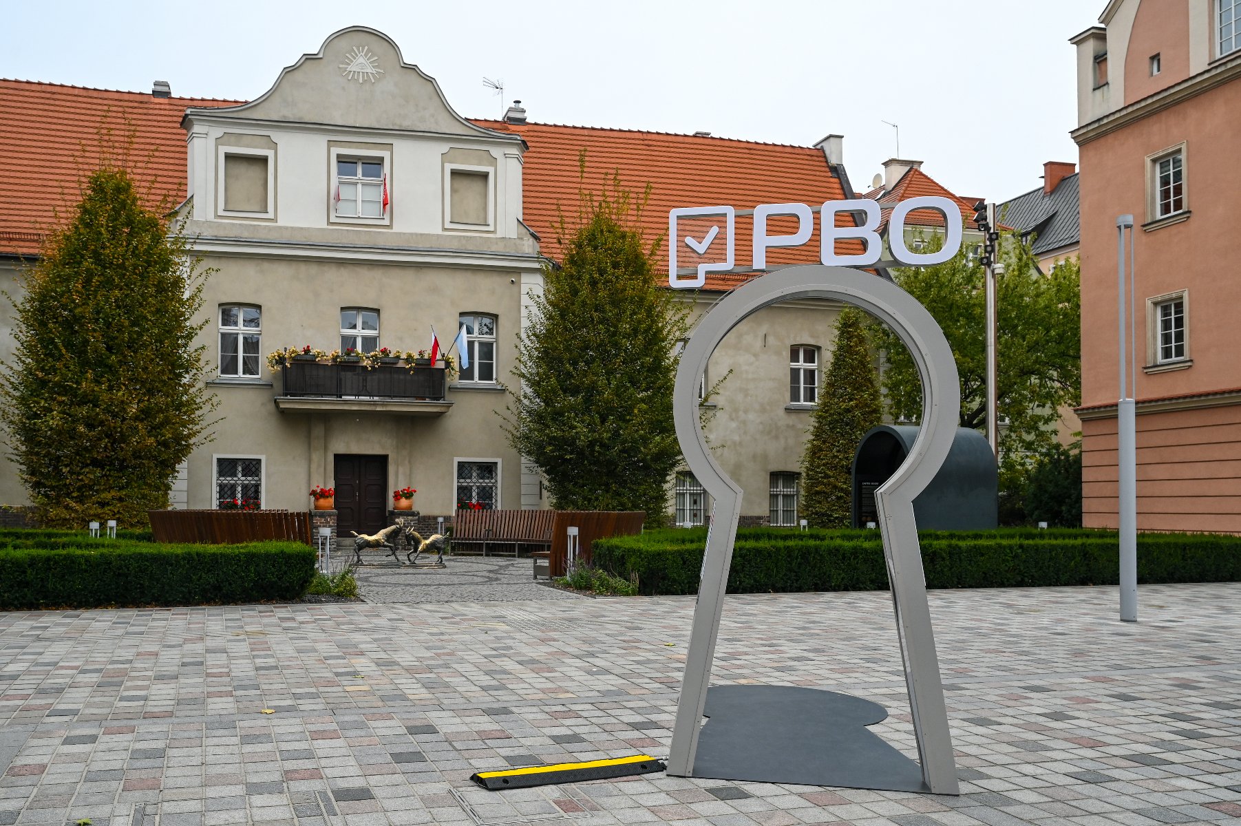 Zdjęcie przedstawia instalację w kształcie dużej dziurki od klucza, stojącej na placu. Na górze tej instalacji znajduje się napis PBO.