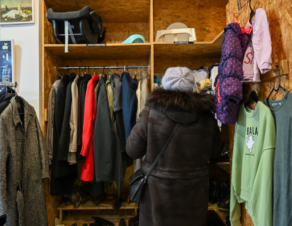 Zdjęcie przedstawia kobietę przeglądającą wieszaki z ubraniami.