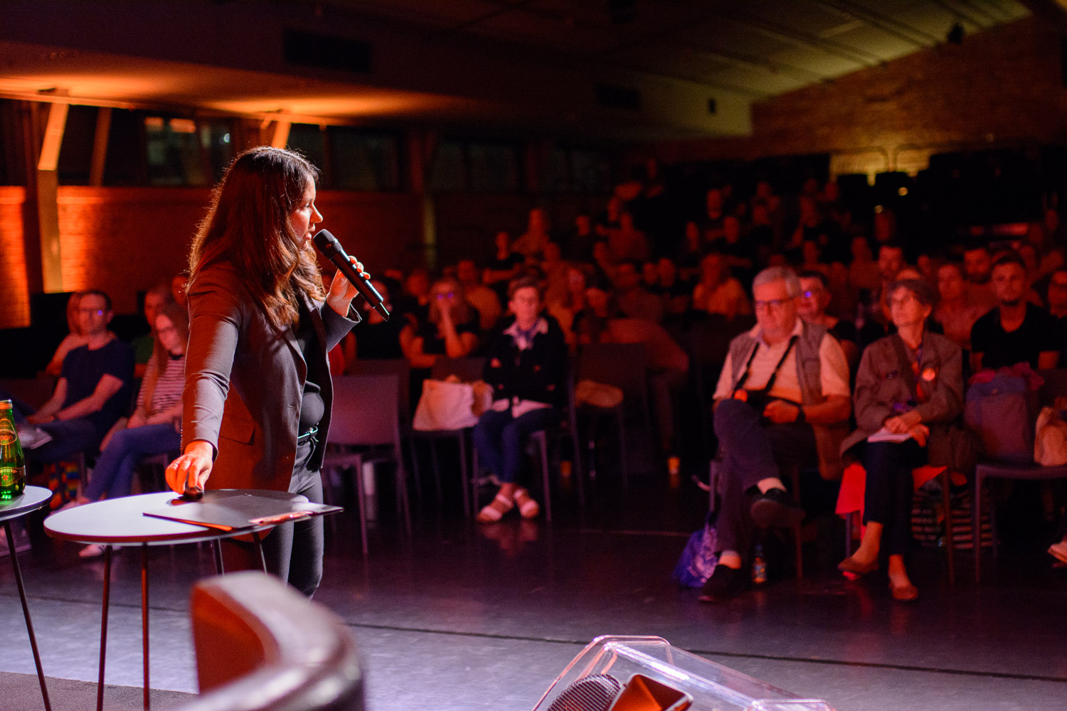 Zdjęcie przedstawia kobietę w białym kaftanie i kapturze na głowie, która w jednej ręce trzyma czaszkę, a w drugiej książkę.
