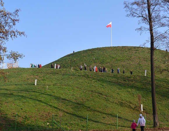 Zdjęcie przedstawia Kopiec Wolności i zwiedzajacych go ludzi.
