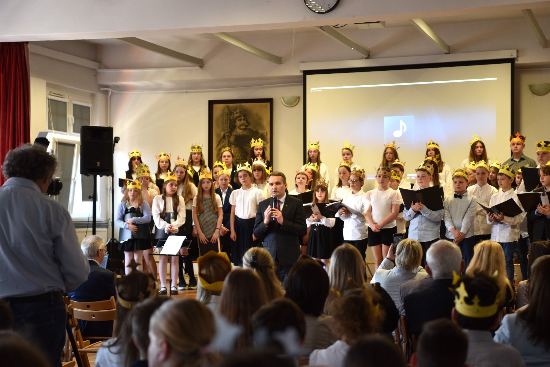 Zdjęcie przedstawia małą sadzonkę drzewka w ziemi oraz tabliczkę ją opisującą. Dalej widać wbitą w ziemię łopatę.