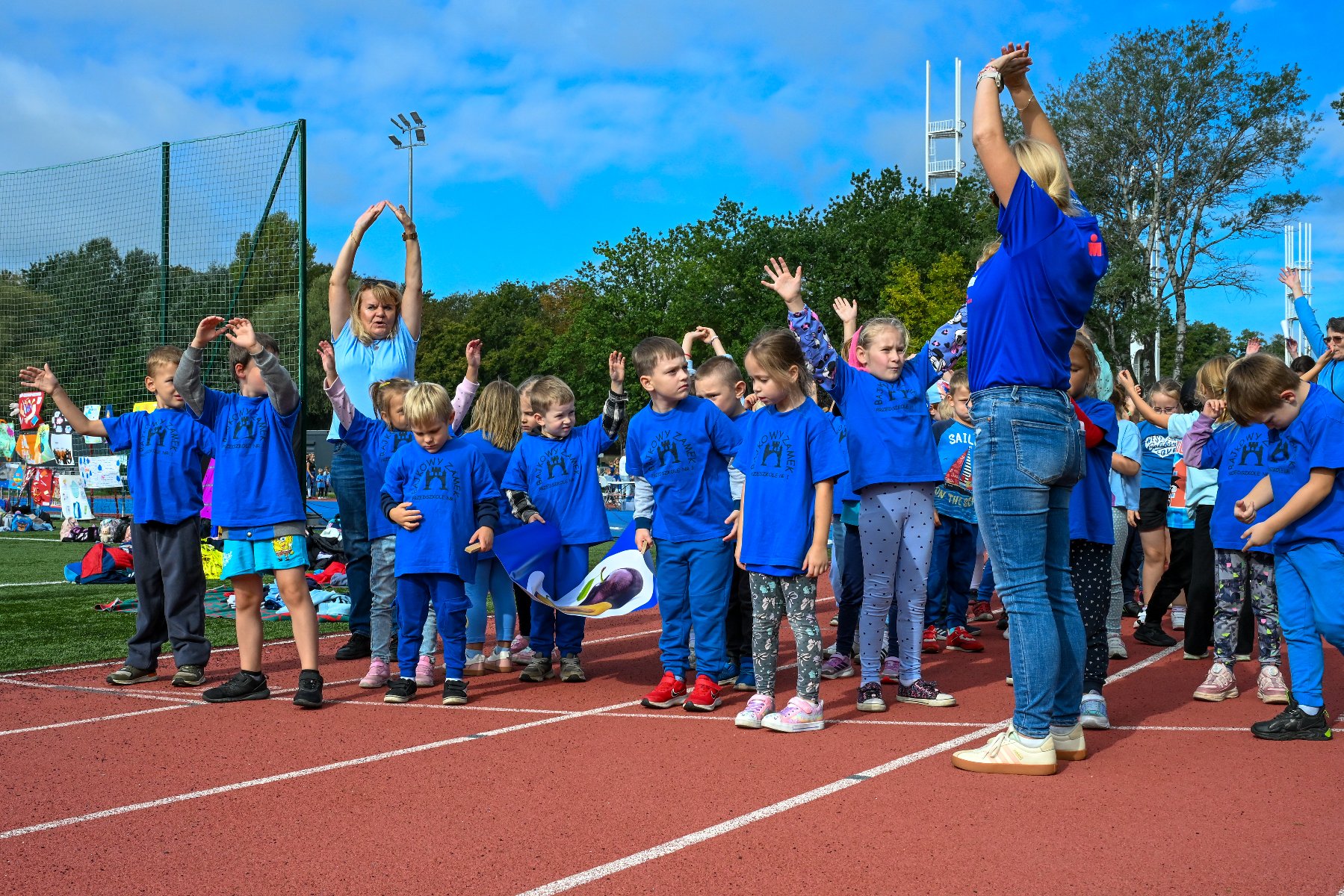 Zdjęcie przedstawia medale z wizerunkiem biegnącego jabłka i napisem Ogólnopolski Dzień Przedszkolaka. Za nimi w tle widać biegnące dzieci.