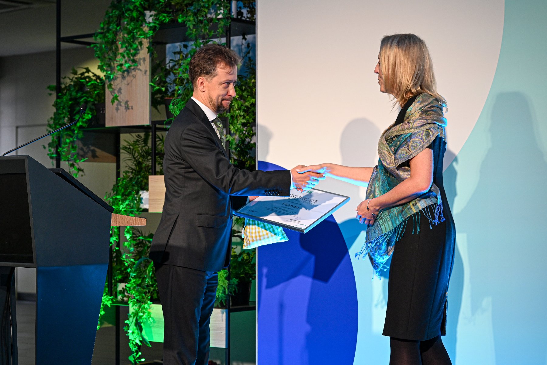 Zdjęcie przedstawia mężczyznę przekazującego dyplom kobiecie.