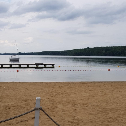 Miejska plaża nad Jeziorem Kierskim/ fot. POSiR Zdjęcie przedstawia miejską plażę. Na jeziorze widać pomost i statek.
