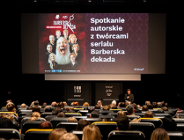Zdjęcie przedstawia salę kinową. Na krzesłach siedzą młodzi ludzi, a na ekranie jest informacja o serialu i spotkaniu autorskim.