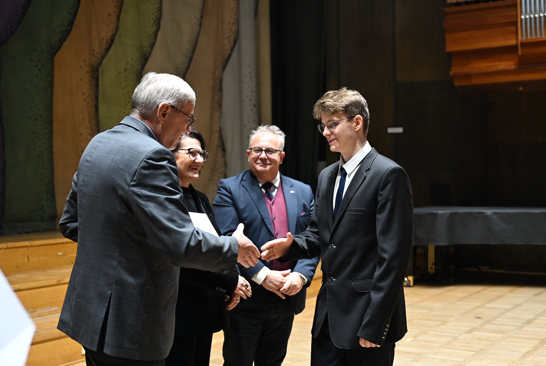 Zdjęcie przedstawia starszego mężczyznę wręczającego dyplom młodej dziewczynie.