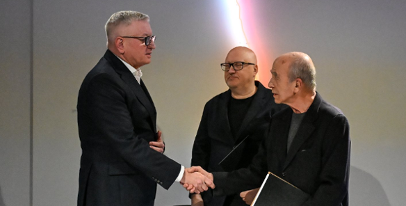 Zdjęcie przedstawia trzech mężczyzn. Dwóch podaje sobie ręke.