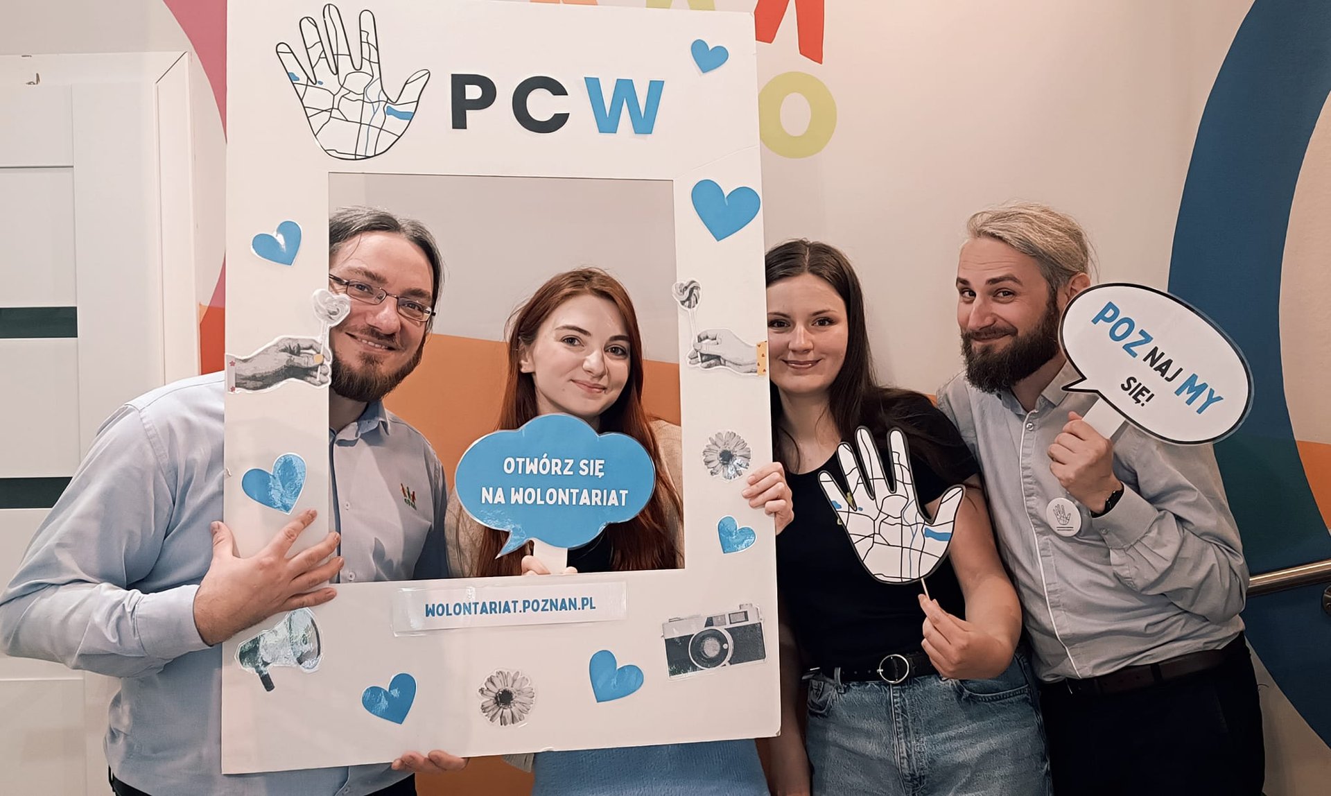 zdjęcie przedstawia uśmiechniętych pracowników Stowarzyszenia CREO - cztery osoby, w tym dwie kobiety i dwóch mężczyzn. Osoby trzymają w rękach ramkę do zdjęć oraz plakietki z napisami związanymi z wolontariatem