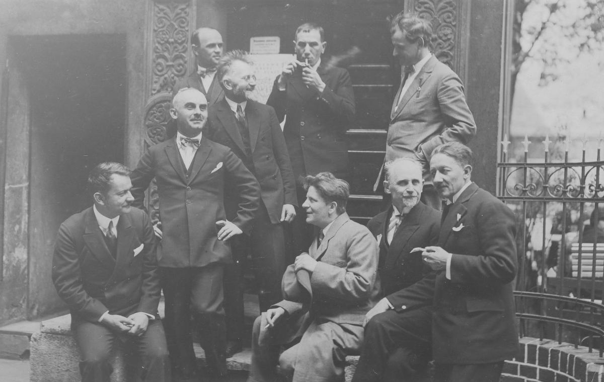 Zdjęcie sprzed 100 lat, grupa mężczyzn siedzi, stoi, rozmawiają palą