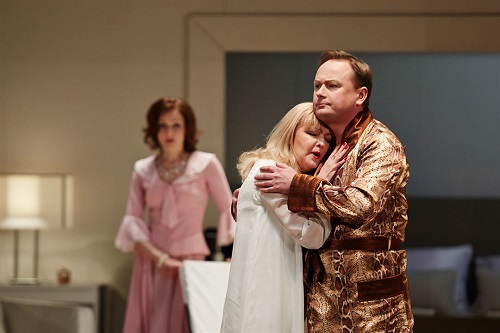 Na pierwszym planie obejmująca się para - kobieta w koszuli nocnej, mężczyzna w szlafroku. W tle kobieta w rózowej sukience, która na nich patrzy.