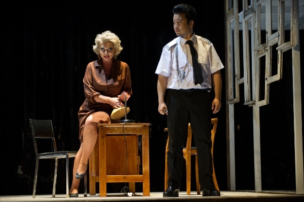 Zdjęcie kobiety siedzącej na biurku, obok niej stoi mężczyzna w białej koszuli, krawacie i ciemnych spodniach.