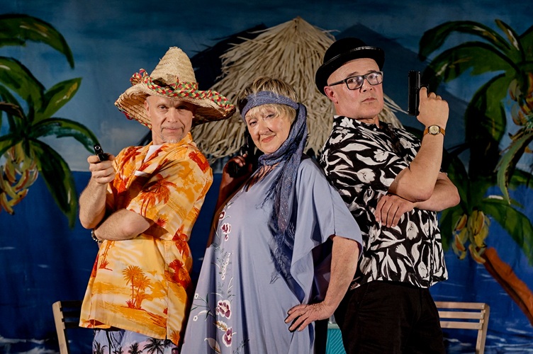 Dwóch mężczyzn i jedna kobieta, stoją obok siebie i patrzą w obiektyw. Ubrani sa w kolorowe stroje, jeden z mężczyzn trzyma mały pistolet.