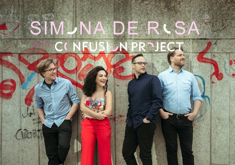 Czworo osób stoi przy betonowej ścianie pokrytej czerwonym graffiti. Trzech mężczyzn i jedna kobieta uśmiechają się i patrzą w jedną stronę. Na górze obrazu widnieje napis w różowo-białym kolorze: "Simona De Rosa, Confusion Project".