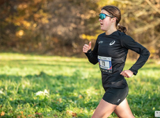 Zwyciężczyni pierwszego w nowym sezonie biegu City Trail w Poznaniu, fot. Piotr Oleszak - na tle trawy i lasu biegnie kobieta w czarnym stroju