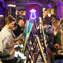 Grupa osób maluje obrazy na sztalugach.