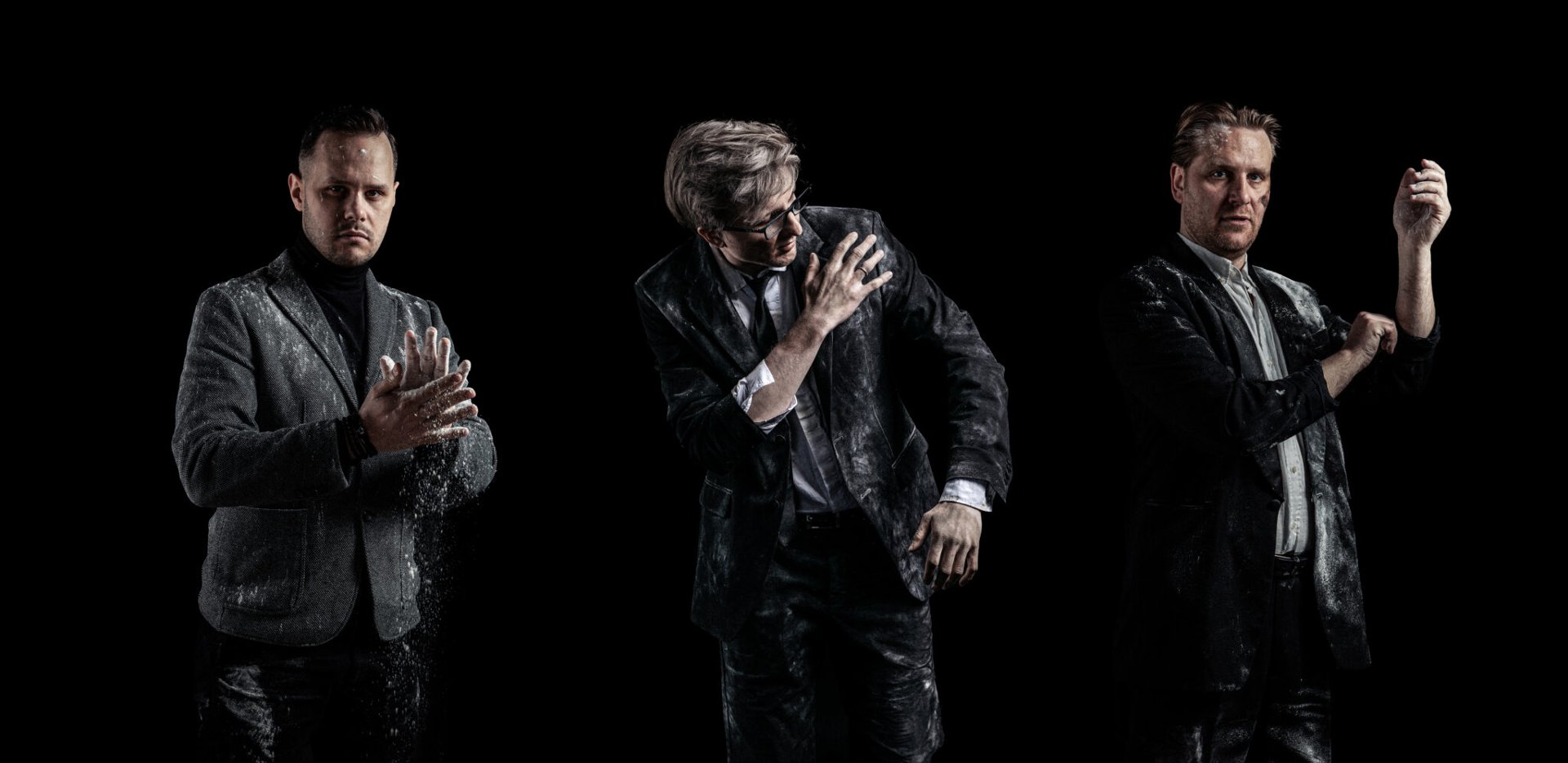 Trzech mężczyzn w ciemnych garniturach i marynarkach pozuje na czarnym tle. Ich ubrania, twarze i dłonie są mocno pobrudzone białym proszkiem przypominającym mąkę lub pył. Mężczyzna po lewej klaszcze w dłonie, wzbijając chmurę pyłu, środkowy otrzepuje ramię, a ten po prawej podwija rękaw.