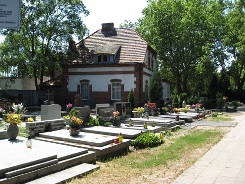 Budynek biura cmentarza Górczyńskiego. Obok groby. W głębi drzewa.