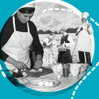 Czarno-białe zdjęcie kobiety w trakcie gotowania. W tle Para w strojach narodowych i kucharz.