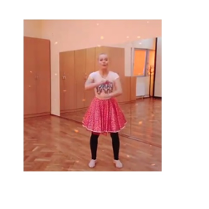 Kobieta w stroju baletnicy, w różowej spódnicy, jasnej koszulce i czarnych getrach, w sali ze ścianą z luster.