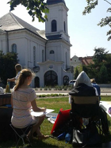 Latu. Uczestnicy kursu widziani z tyłu w plenerze szkicują kosciół Wszystkich Świetych na Grobli w w Poznaniu.