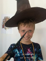 Uśmiechnięty chłopiec w kapeluszu czarodzieja z różdżką w dłoni.