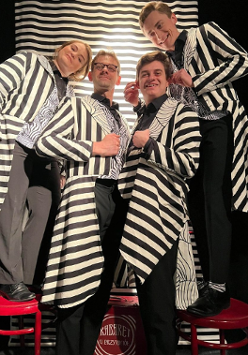 Zdjęcie aktorów - kobieta i trzech mężczyzn we frakach w biało-czarne paski. Stoją obok siebie, wpatrzeni w obiektyw, uśmiechają się.