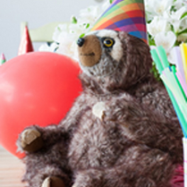 Leniwiec w kolorowej czapeczce obok czerwony balonik