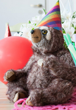 Leniwiec w kolorowej czapeczce obok czerwony balonik.