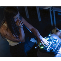 Na zdjęciu młoda dziewczyna siedzi przy konsoli didżejskiej, w ręce trzyma mikorofon, coś mowi.