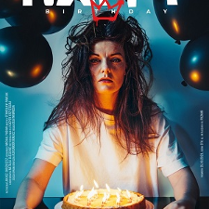 Kobieta z długimi, potarganymi włosami patrzy w obiektyw aparatu. Przed nią tort z zapalonymi świeczkami, nad głową czarne balony oraz tytuł przedstawienia.