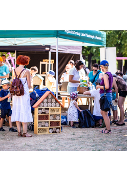 Stoisko na dworze, dookoła dorośli i dzieci, na pierwszym planie domek dla owadów