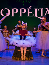 Na scenie dziewczynki przebrane za baletnice. Mają kolorowe gorsety z motywem kwiatowym oraz tiulowe spódnice. W tle zielone tło z napisem "Coppelia".