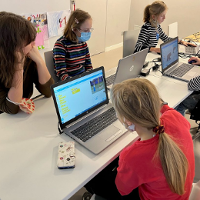 Zdjęcie przedstawia dzieci siedzące wspólnie przed monitorem w trakcie zajęć komputerowych.