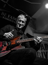 Mężczyzna na scenie pokazuje gest kciuka w górę grając na gitarze.