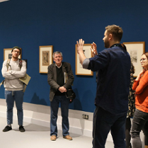 Grupa osób zwiedza wystawę z osobą prowadzącą