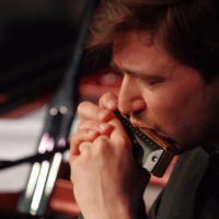 Zdjęcie twarzy mężczyzny grającego na harmonijce.