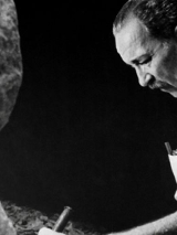 Na czarno-białym zdjęciu artysta rzeźbiący w kamieniu.