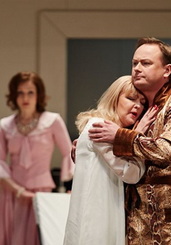 Na pierwszym planie obejmująca się para - kobieta w koszuli nocnej, mężczyzna w szlafroku. W tle kobieta w rózowej sukience, która na nich patrzy.