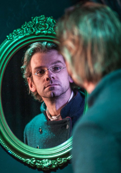 Zdjęcie mężczyzny przeglądającego się w lustrze ze zdobioną ramą.